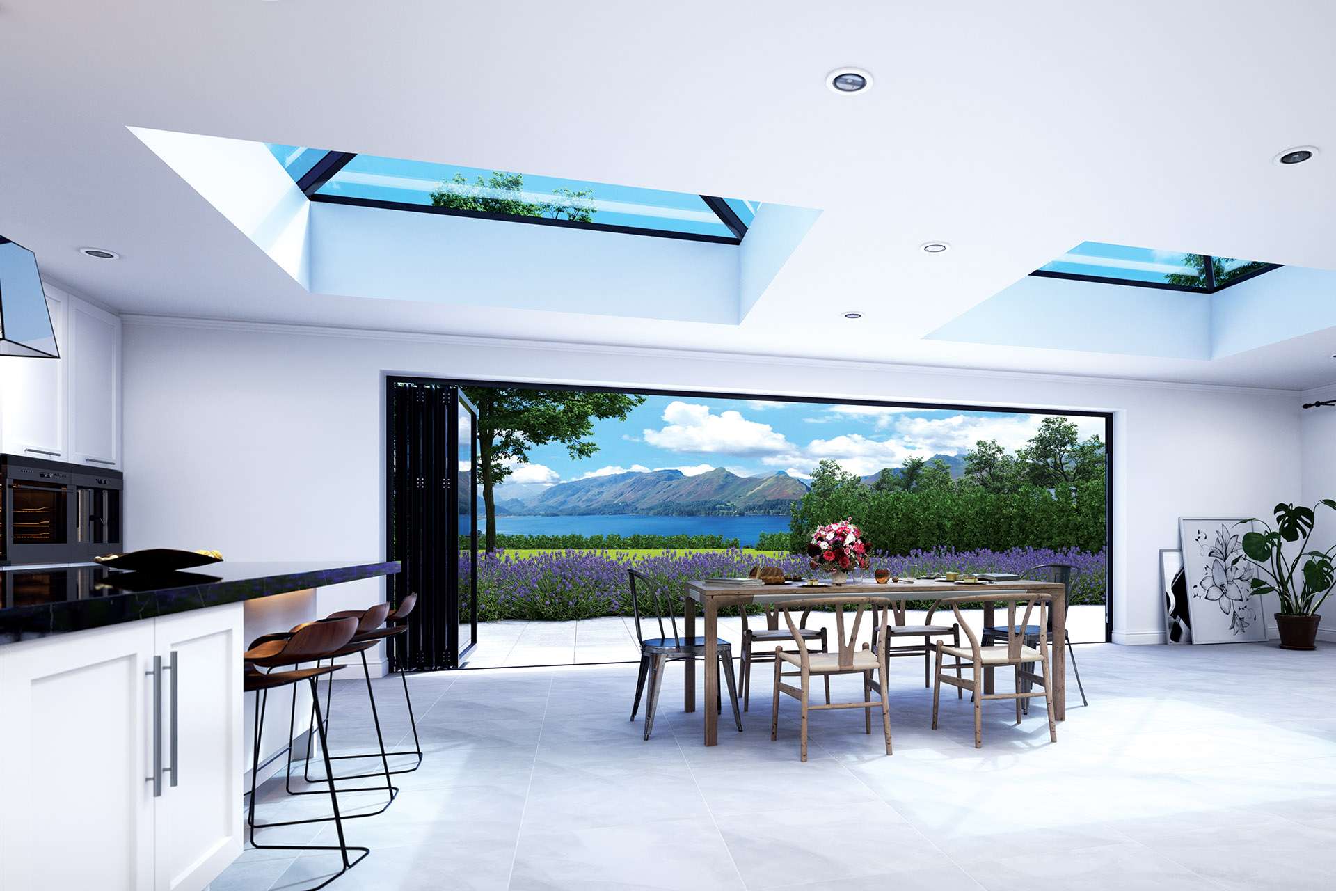 A wide shot of a fully furnished kitchen that has two Korniche roof lanterns installed one on the left and one on the right. A set of Korniche bi-folding doors open up fully onto a view of a field of flowers, the lake and mountains in the distance.